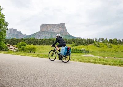 Une femme à vélo avec des sacoches devant le Mont Aiguille dans le Trièves et Vercors - Photo © Florian Garibal