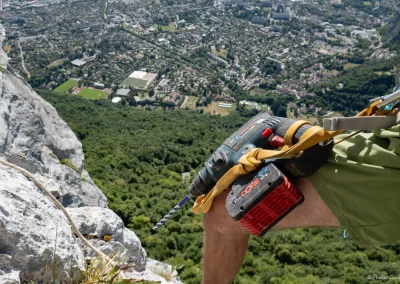 Une personne équipe une grande voie d'escalade en falaise avec un perfo - Photo © Florian Garibal